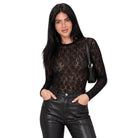 A woman modeling a black sheer lace long-sleeve top paired with black faux-leather pants, standing against a plain white background.