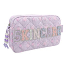 A light purple quilted cosmetic pouch with a floral pattern, featuring the word 'SKINCARE' spelled out in glittery, pastel-colored letters across the front. The pouch has a zipper closure with a purple and white beaded tassel zipper pull on the left side.