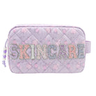 A light purple quilted cosmetic pouch with a floral pattern, featuring the word 'SKINCARE' in glittery, multicolored letters across the front. A lavender drawstring bag clip is visible on the left side.