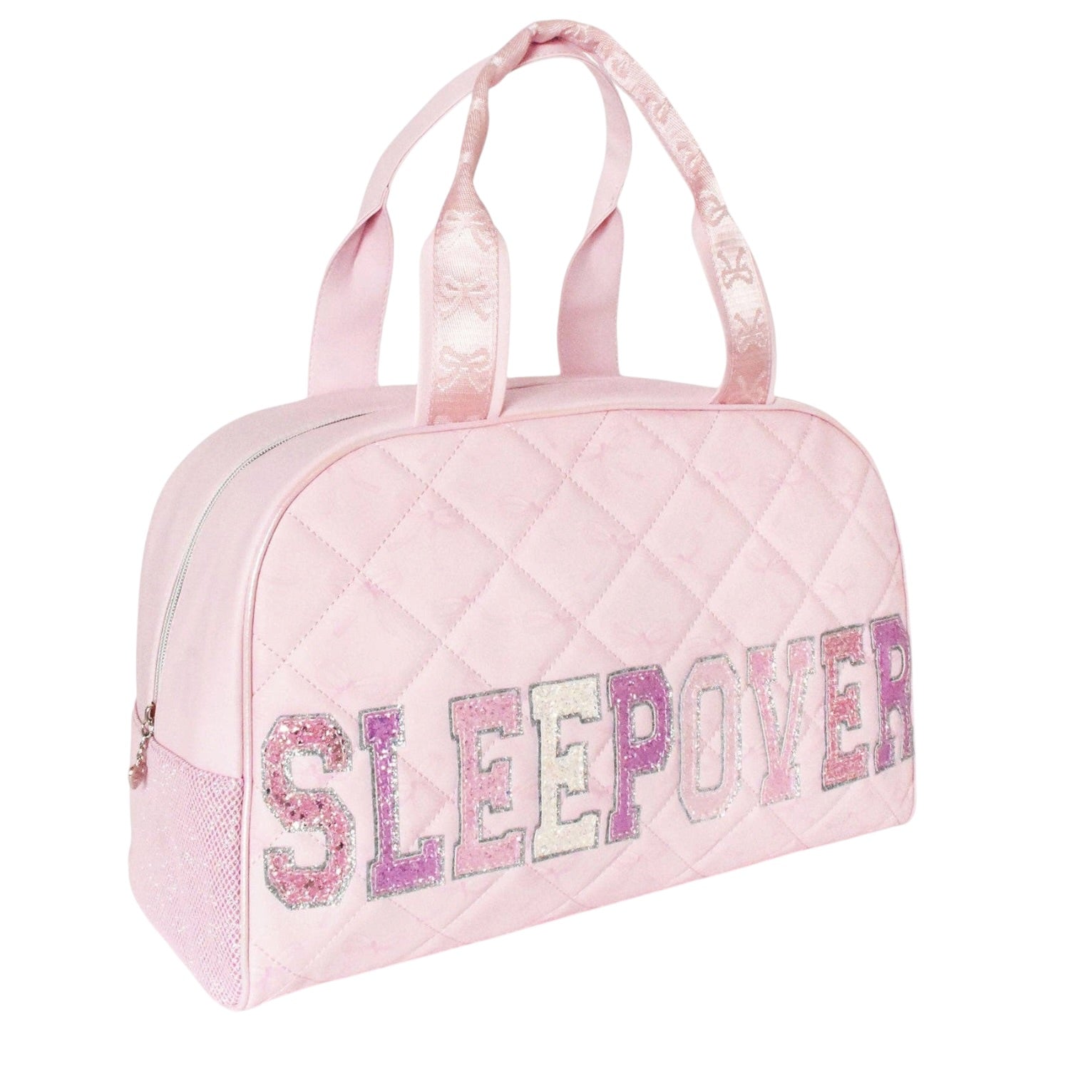 A light pink quilted duffel bag with 'SLEEP OVER' written across the front in glittery pink, purple, and white letters, featuring two top handles on a white background.