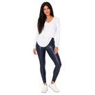A woman modeling a white long-sleeve V-neck top and shiny dark navy leggings with white sneakers, standing against a plain white background.