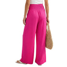 Person wearing bright pink wide-leg pants holding a beaded bag on a white background