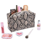 A zippered cosmetic bag with a beige and black snakeskin pattern, shown open with makeup items inside and several makeup products arranged around it on a white background.