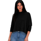 A woman modeling a black mock-neck knit sweater with three-quarter sleeves and ribbed cuffs, paired with blue jeans, against a plain white background.