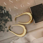 Gold hoop earrings on a surface with 'Hanging Things' book in the background