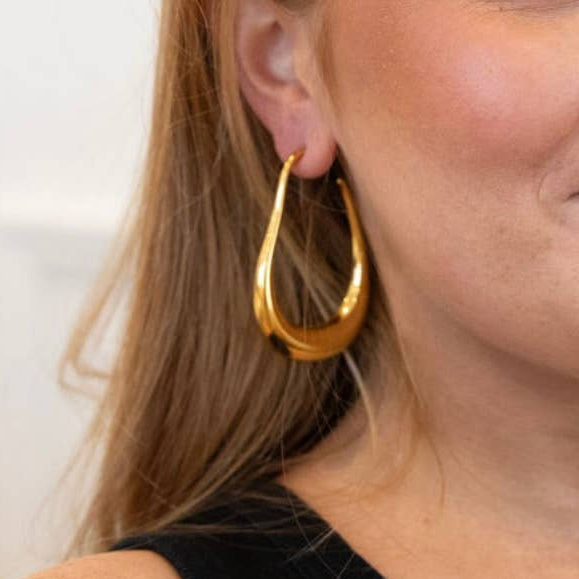 Woman with long blonde hair and gold hoop earrings posing against a white background