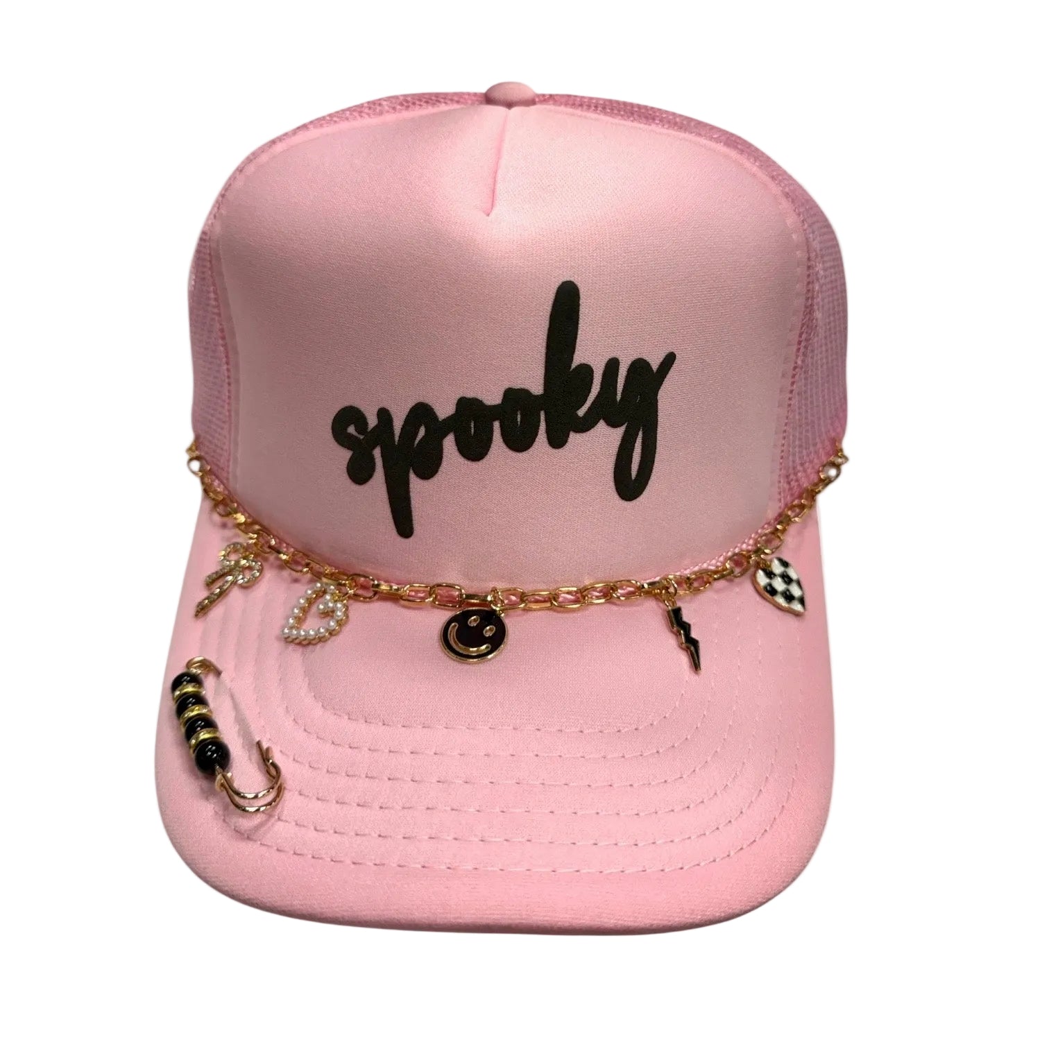 A pink trucker hat with 'spooky' written in black script on the front, decorated with a gold chain and various small black and white charms, including a checkered heart and a beaded ring, against a light gray background.