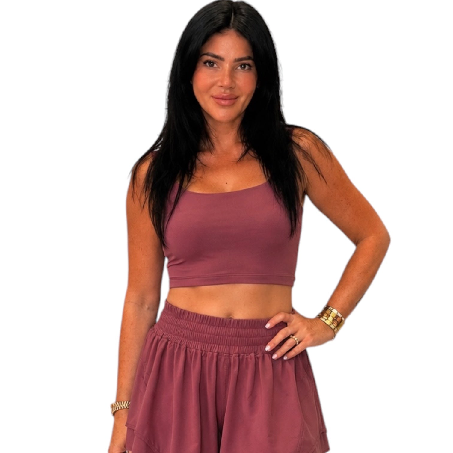 A woman modeling a matching dusty rose two-piece activewear set consisting of a cropped tank top and a high-waisted skort, set against a plain white background.