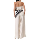 Woman wearing a white halter jumpsuit with a black and white striped sash on a white background