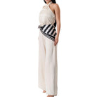 Woman wearing a white halter neck jumpsuit with black and white striped belt on a white background