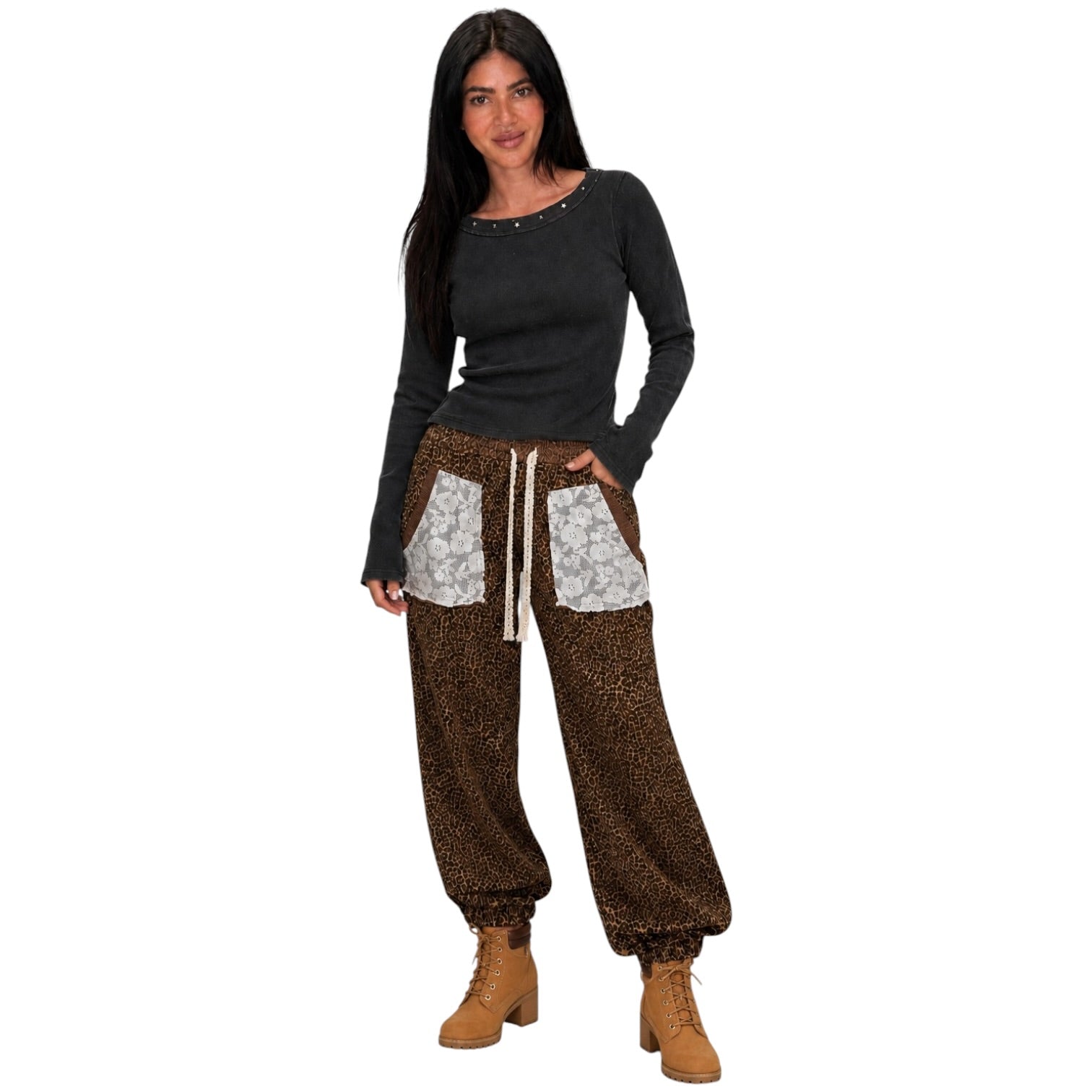 A woman modeling a pair of brown leopard-print harem pants with light gray patterned front patch pockets and a cream drawstring, paired with a dark charcoal long-sleeve top and tan lace-up boots, against a plain white background.