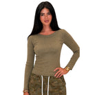 A woman modeling a fitted, long-sleeve crew-neck top in olive green with small silver stud embellishments around the neckline, paired with camouflage drawstring pants against a plain white background.