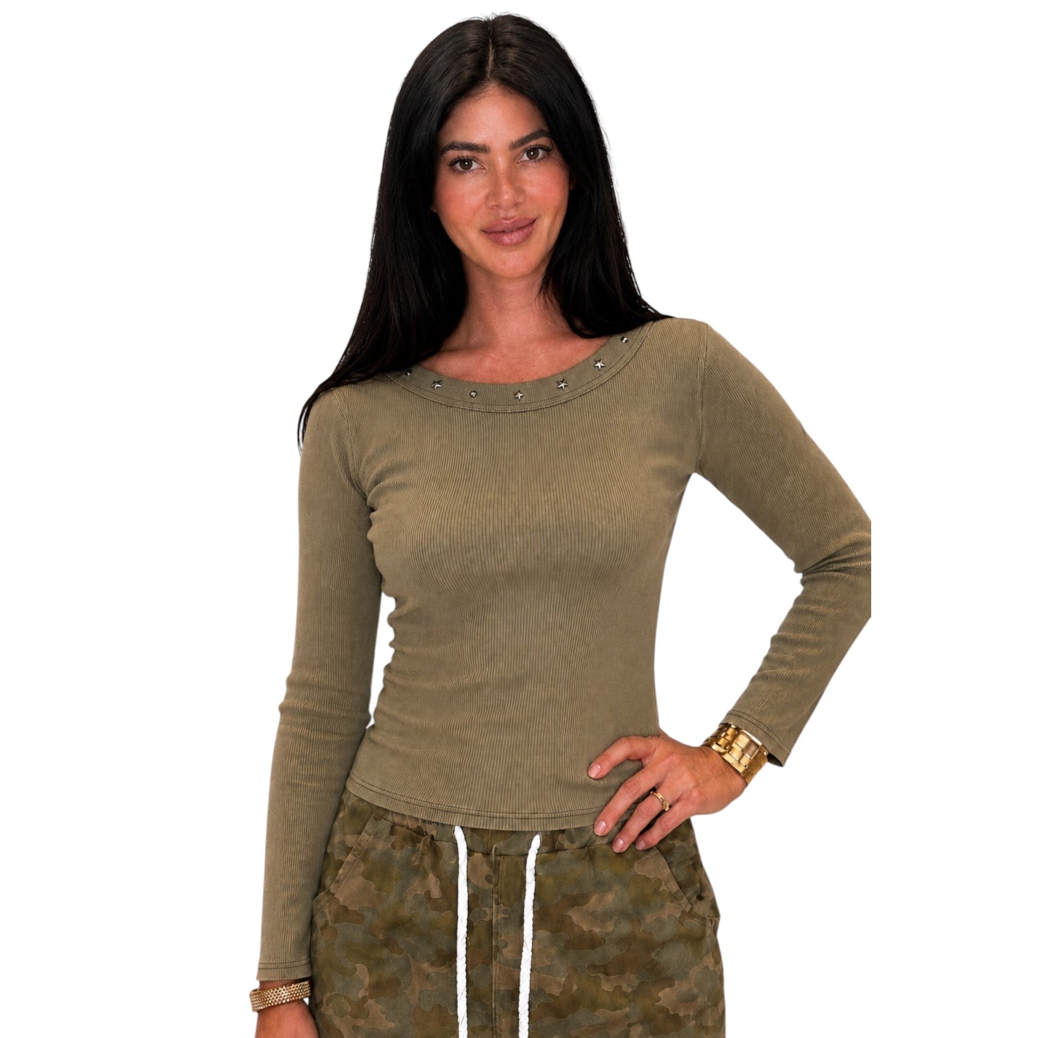 A woman modeling a fitted, long-sleeve crew-neck top in olive green with small silver stud embellishments around the neckline, paired with camouflage drawstring pants against a plain white background.
