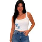 Woman wearing a white tank top with blue starfish designs and blue jeans on a white background