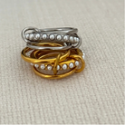 Two rings, one silver and one gold, with pearl accents on a beige fabric background.