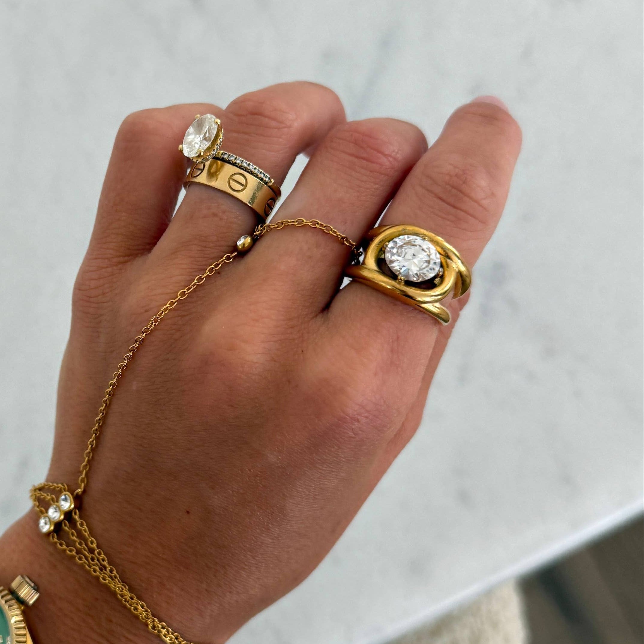 Hand wearing multiple gold rings and a bracelet on a light background