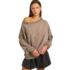 Woman wearing a beige off-shoulder sweatshirt with a plain background