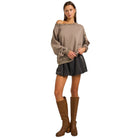 Woman wearing a beige sweater, black skirt, and brown knee-high boots on a white background
