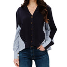 A woman wearing a cardigan with a dark navy body and light blue and white striped sleeves, paired with dark blue jeans, against a plain white background.