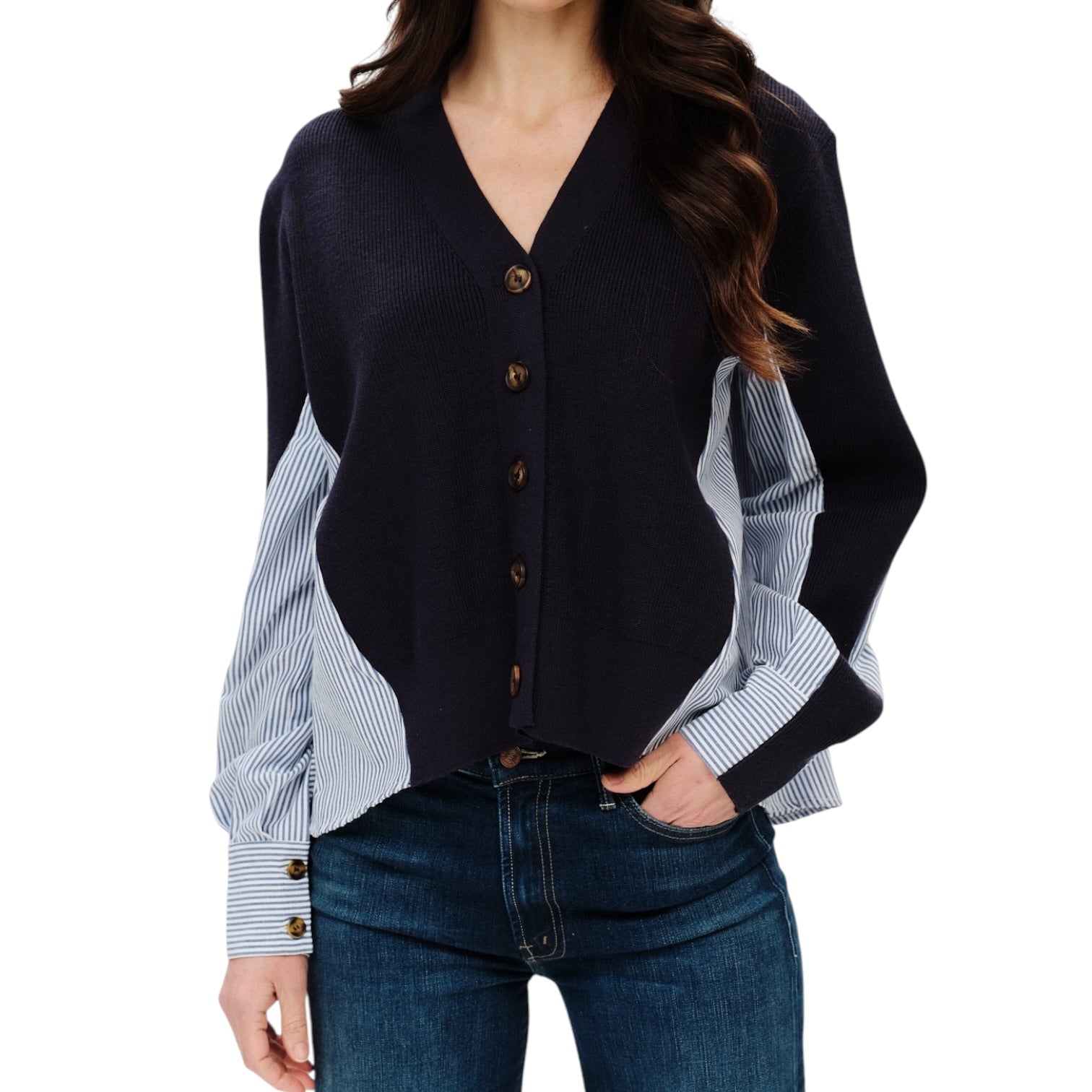 A woman wearing a cardigan with a dark navy body and light blue and white striped sleeves, paired with dark blue jeans, against a plain white background.