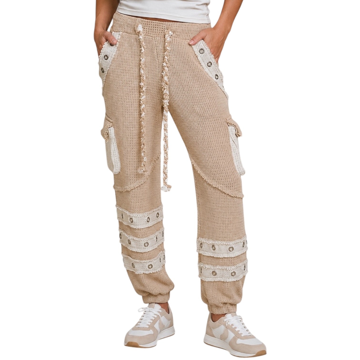 A person wearing beige textured knit cargo jogger pants with cream lace trim, decorative eyelet bands, and a drawstring waist, paired with white sneakers against a plain white background.