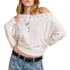 Woman wearing a white off-shoulder top with embellishments and blue jeans on a white background