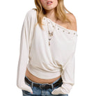 Woman wearing a white off-shoulder top with pearl embellishments on a white background