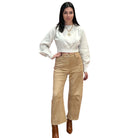 Woman wearing a off white long-sleeve sweater and camel suede barrel pants on a white background