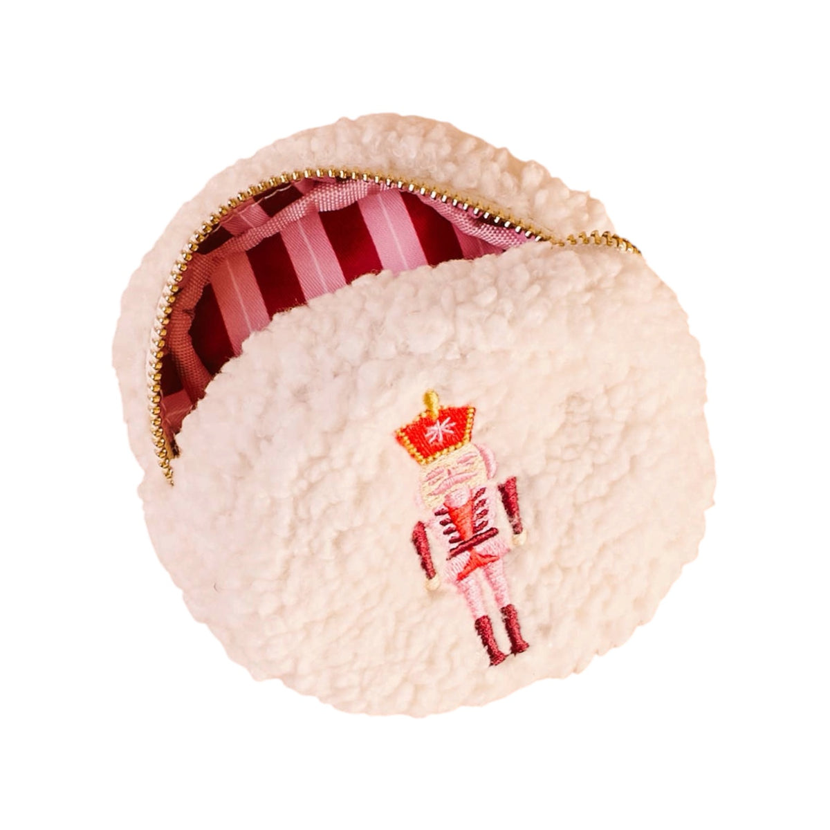 A round, cream-colored faux-shearling pouch with a gold zipper, featuring an embroidered nutcracker figure on the front and a pink and white striped lining visible inside.