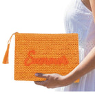 Orange clutch bag with 'Supreme' branding held by a person wearing a white dress.