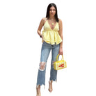 Woman wearing a yellow top and blue jeans, holding a yellow handbag on a white background
