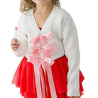 Young girl wearing a white cardigan, red skirt with a pink bow, and beige tights on a white background