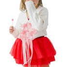 Young girl in a red skirt and white sweater holding a pink flower against a white background