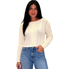 Woman wearing a cream sweater and blue jeans on a white background