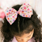 Child wearing a colorful bow in their hair with a heart pattern.