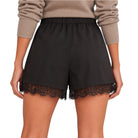 Black high-waisted shorts with a lace hem, shown on a model wearing a beige ribbed sweater against a white background.