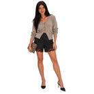 A woman modeling a taupe knit cardigan with a front button placket and side cutouts, paired with black lace-trimmed shorts and black high heels, holding a zebra-print clutch against a plain white background.