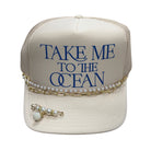 Beige cap with 'Take Me to the Ocean' text and pearl and chain accessories on a white background