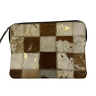 A rectangular zip-around clutch bag made of patchwork cowhide in shades of brown, beige, and white, with small scattered gold leaf accents, shown on a plain white background.