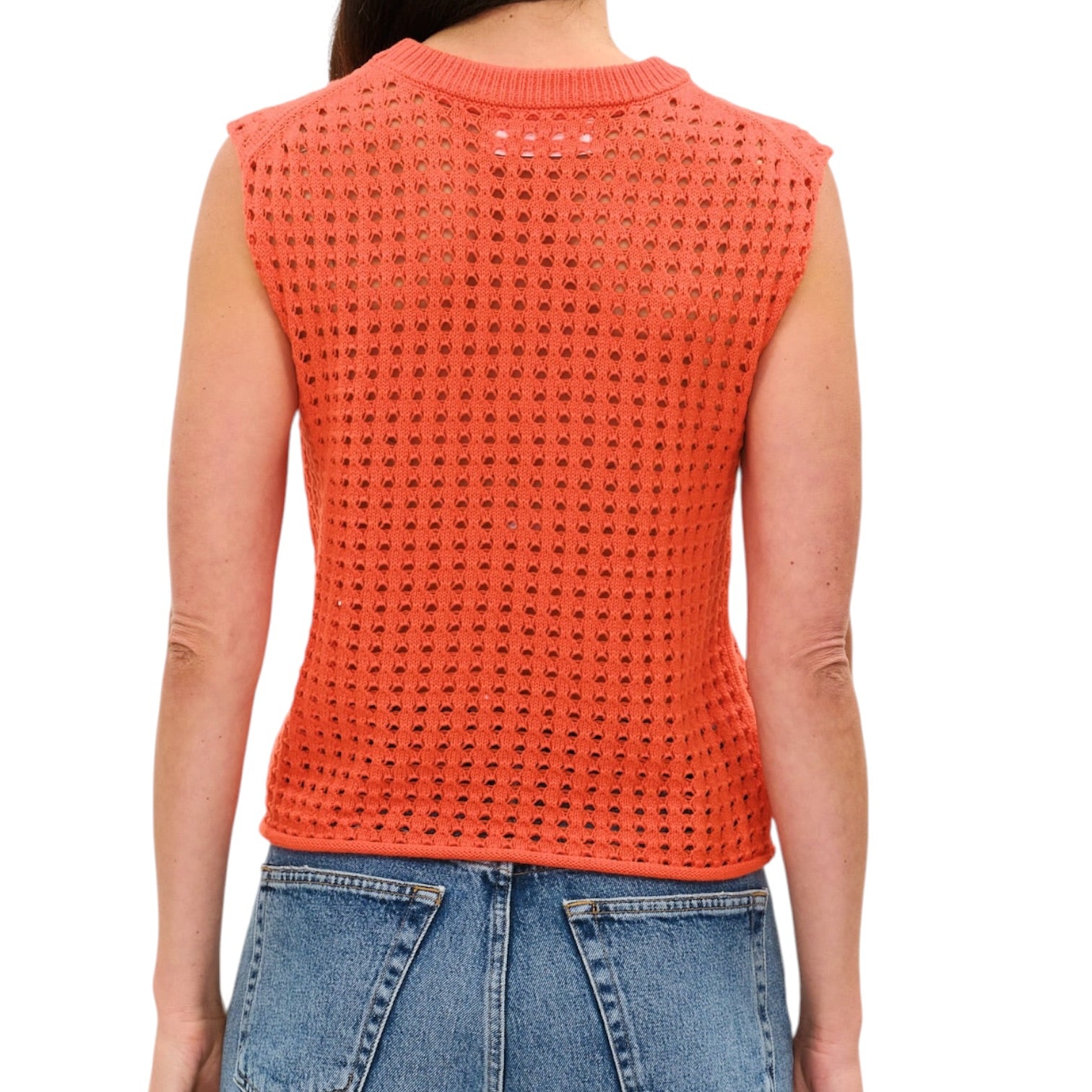 Person wearing an orange sleeveless knitted top and blue jeans on a white background