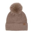 A taupe brown knit beanie hat featuring a large matching faux fur pom-pom on top and a small brown leather 'CC' logo patch on the folded cuff, shown against a plain white background.