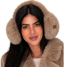 A woman wearing fluffy faux-fur earmuffs in a light taupe-brown color, paired with a matching faux-fur collar. The background is solid white.