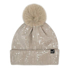 A beige knit pom-pom beanie covered in small silver sequins, featuring a fluffy beige faux-fur pom-pom and a small black 'cc' logo patch on the folded cuff.