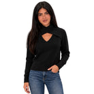 A woman modeling a black long-sleeve knit top with a crossover collar and V-shaped chest cutout, paired with blue jeans, against a plain white background.