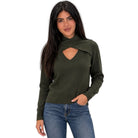 A woman modeling an olive green knit sweater with a unique wrap-around collar and keyhole cutout at the chest, paired with blue jeans against a plain white background.