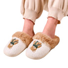 A person wearing fluffy cream-colored slip-on slippers with tan faux-fur trim and embroidered teddy bear faces with green bows, shown against a plain white background.