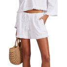 Person wearing white shorts and a white top with a woven bag on a white background