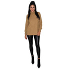 A woman modeling a camel-colored ribbed turtleneck sweater paired with black faux-leather leggings and black ankle boots, set against a plain white background.