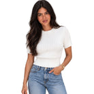 A woman modeling a short-sleeve white ribbed knit top with light blue jeans against a plain white background.