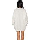 A woman viewed from the back wearing an oversized cream-colored mock-neck sweatshirt dress, set against a plain white background.